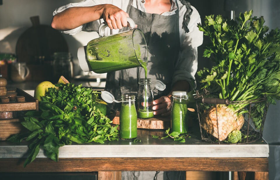 Woman pouring green smoothies into glass jars.